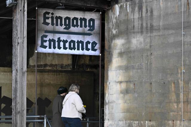The entrance to the Berlin Story Bunker is seen as people walk under a sign reading 'Eingang' during a press presentation of the "Ukraine Museum" in the "Berlin Story Bunker" on February 23, 2026 in Berlin, one day before the exhibition's opening to the public and the fourth anniversary of Russia's invasion in Ukraine. Covering 300 square meters, the former World War II bunker in Berlin's Story Bunker will display various Russian combat drones and a destroyed Ukrainian evacuation vehicle. (Photo by RALF HIRSCHBERGER / AFP)