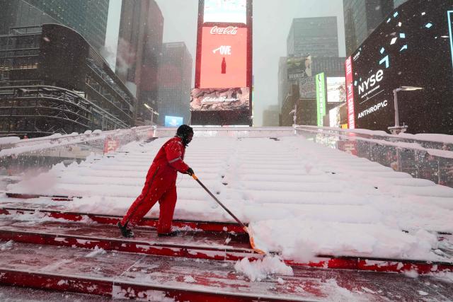 A worker clears the snow on the Red Steps in Times Square during a winter storm in the Manhattan borough of New York City on February 23, 2026. New York ordered drivers off the road and shut down schools on Monday, while residents hunkered down for a massive snowstorm hitting the United States northeast. The National Weather Service (NWS) said in a post on X that "heavy snow is still falling" at 5:28 am local time (1028 GMT) on Monday adding that a the total snowfall stands at 14.9 inches. (Photo by TIMOTHY A.CLARY / AFP)