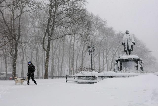 A person walks a dog through a snow-covered park in the Brooklyn borough of New York City on February 23, 2026. New York ordered drivers off the road and shut down schools on Monday, while residents hunkered down for a massive snowstorm hitting the United States northeast. The National Weather Service (NWS) said in a post on X that "heavy snow is still falling" at 5:28 am local time (1028 GMT) on Monday adding that a the total snowfall stands at 14.9 inches. (Photo by ANGELA WEISS / AFP)