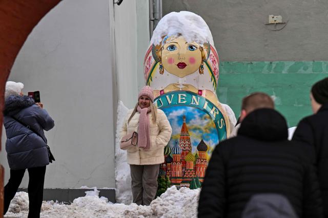 A woman poses for a picture next to a souvenir shop in central Moscow during the Defender of the Fatherland Day on February 23, 2026. (Photo by Hector RETAMAL / AFP)