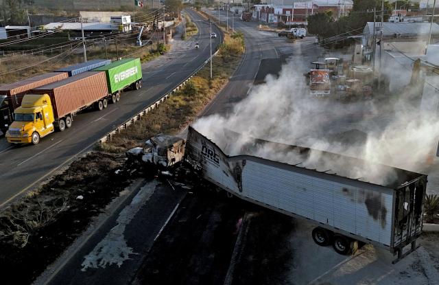 This aerial view shows a burned truck, allegedly set on fire by organised crime groups in response to an operation to arrest a high-priority security target, on a highway near Acatlan de Juarez, Jalisco state, Mexico on February 22, 2026. The Mexican army announced that it had killed powerful drug lord Nemesio "El Mencho" Oseguera in an operation that sparked a wave of violence in various parts of the country on February 22, 2026. Gunmen retaliating for the raid blocked more than 20 roads in western Jalisco state, which includes Tapalpa, with burning cars and trucks. The violence spread to other states as well. (Photo by Ulises Ruiz / AFP)