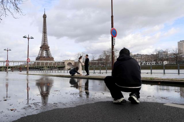 Two people pose for a photograph with wedding outfits on a flooded banks of the Seine river with the Eiffel tower in the background, in Paris on February 23, 2026. (Photo by Ludovic MARIN / AFP)