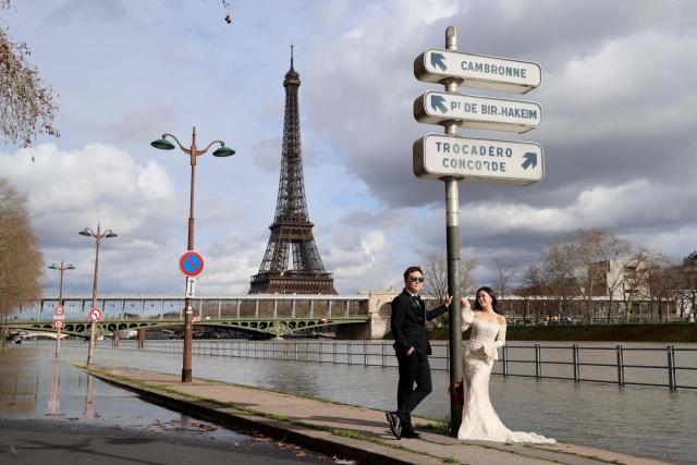 Two people pose for a photograph with wedding outfits on a flooded banks of the Seine river with the Eiffel tower in the background, in Paris on February 23, 2026. (Photo by Ludovic MARIN / AFP)