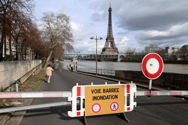 A person goes down a closed access to the flooded banks of the Seine river with the Eiffel tower in the background, in Paris on February 23, 2026. (Photo by Ludovic MARIN / AFP)