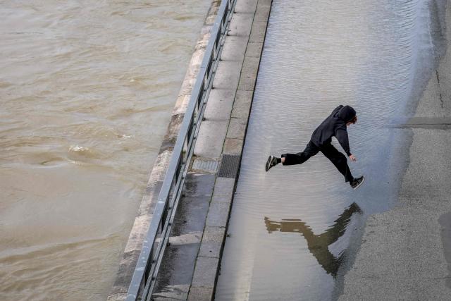 A boy jumps over water on a flooded bank of the Seine river in Paris on February 23, 2026. (Photo by Ludovic MARIN / AFP)