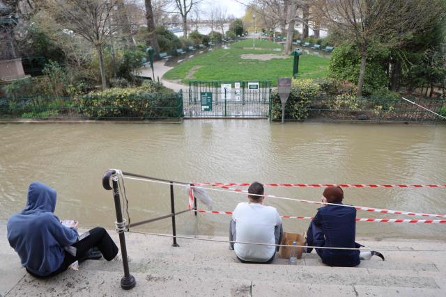 People sit on stairs in front of the flooded Square du Vert Galant in Paris on February 23, 2026. (Photo by Ludovic MARIN / AFP)