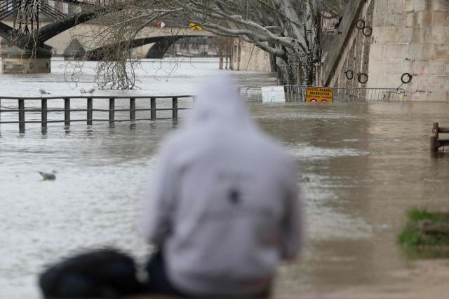 A person sits in front of a flooded bank of the Seine river in Paris on February 23, 2026. (Photo by Ludovic MARIN / AFP)