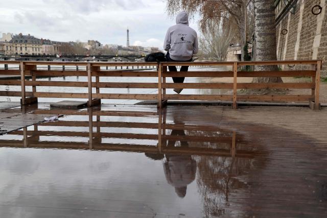 A person sits in front of a flooded bank of the Seine river in Paris on February 23, 2026. (Photo by Ludovic MARIN / AFP)