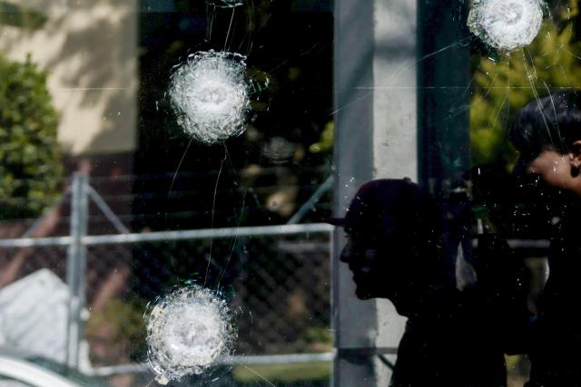 Young men walk past teh window of a police station with bullet impacts in Guadalajara, Jalisco, Mexico, on February 23, 2026, a day after clashes. Mexico has deployed 10,000 troops to quell clashes sparked by the killing of the country's most-wanted drug lord, Nemesio "El Mencho" Oseguera, leader of the Jalisco New Generation Cartel (CJNG), that have claimed dozens of lives, officials said on February 23. News of his death triggered spasms of violence, with cartel members blocking roads in 20 states and torching vehicles and businesses. (Photo by Ulises RUIZ / AFP)