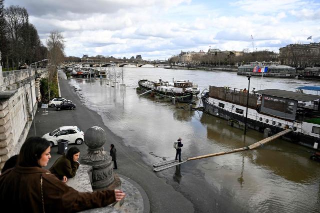 A pedestrian walks on a makeshift pontoon leading to a docked boat accross the flooded banks of the River Seine in Paris on February 23, 2026. (Photo by Anna KURTH / AFP)