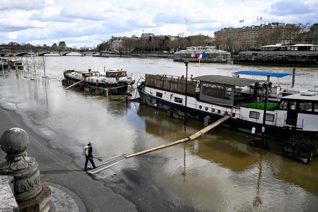 A pedestrian walks on a makeshift pontoon leading to a docked boat accross the flooded banks of the River Seine in Paris on February 23, 2026. (Photo by Anna KURTH / AFP)