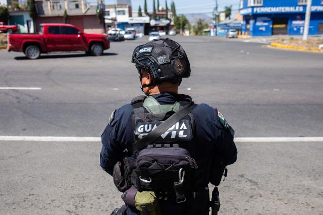 A police officer conducts a security checkpoint on the MoreliaPatzcuaro Highway to prevent vehicle fires and road blockades in Michoacan state, Mexico, on February 23, 2026. Mexico has deployed 10,000 troops to quell clashes sparked by the killing of the country's most wanted drug lord, which have left dozens dead, officials said on February 23. Nemesio "El Mencho" Oseguera, leader of the Jalisco New Generation Cartel (CJNG), was wounded on February 22 in a shootout with soldiers in the town of Tapalpa in Jalisco state and died while being flown to Mexico City, the army said. (Photo by Enrique Castro / AFP)