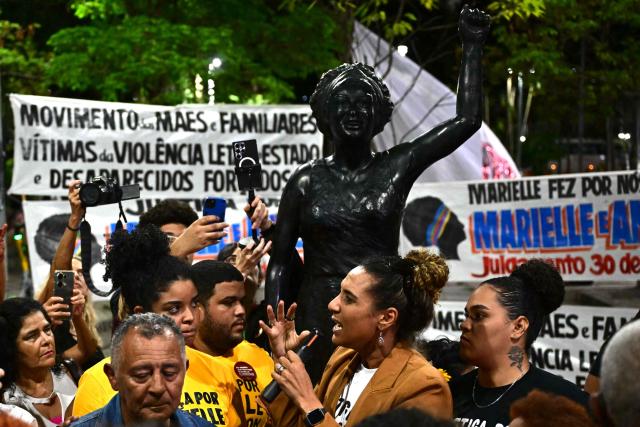 (FILES) Marielle Franco's sister and Minister of Racial Equality, Anielle Franco (R) speaks next to their father Antonio Franco (L) and her niece Luyara Santos in front of a statue in honour of the late activist in Rio de Janeiro downtown, Brazil, on October 31, 2024, after attending the last day of the public trial of the murderers of Marielle and her driver, Anderson Gomes. Eight years after the murder of councilwoman Marielle Franco, an icon of Black and LGBT rights in Brazil, the Supreme Court will begin on February 24, 2026, in Brasilia, a trial of politicians and former police officials accused of ordering the crime. (Photo by Pablo PORCIUNCULA / AFP)