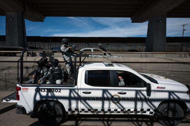 A Mexican National Guard patrol passes past a burned car, allegedly set on fire by organized crime groups, on International Avenue on the Mexican side of the US-Mexico border in Tijuana, Baja California State, Mexico on February 23, 2026. Mexico has deployed 10,000 troops to quell clashes sparked by the killing of the country's most-wanted drug lord, Nemesio "El Mencho" Oseguera, leader of the Jalisco New Generation Cartel (CJNG), that have claimed dozens of lives, officials said on February 23. News of his death triggered spasms of violence, with cartel members blocking roads in 20 states and torching vehicles and businesses. (Photo by Guillermo Arias / AFP)