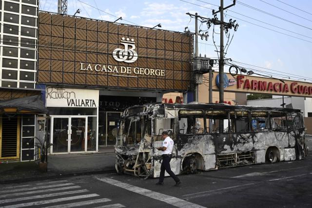 A police officer walks next to a burned?out bus in Puerto Vallarta, Jalisco state, Mexico, on February 23, 2026. Mexico has deployed 10,000 troops to quell clashes sparked by the killing of the country's most wanted drug lord, which have left dozens dead, officials said on February 23. Nemesio "El Mencho" Oseguera, leader of the Jalisco New Generation Cartel (CJNG), was wounded on February 22 in a shootout with soldiers in the town of Tapalpa in Jalisco state and died while being flown to Mexico City, the army said. (Photo by Alfredo ESTRELLA / AFP)