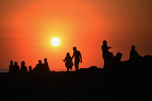 The silhouettes of tourists enjoying El Tunco Beach are seen during the sunset in La Libertad, El Salvador, on February 13, 2026. Amid picture-perfect waves and sunsets, foreign tourists enjoy the Salvadoran beach of El Tunco, once plagued by gang violence. They are full of praise for President Nayib Bukele, even though they admit that innocent people may have been caught up in his crackdown. (Photo by Marvin RECINOS / AFP)
