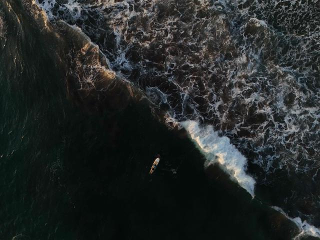 This aerial view shows a person surfing at El Tunco Beach in La Libertad, El Salvador, on February 13, 2026. Amid picture-perfect waves and sunsets, foreign tourists enjoy the Salvadoran beach of El Tunco, once plagued by gang violence. They are full of praise for President Nayib Bukele, even though they admit that innocent people may have been caught up in his crackdown. (Photo by Marvin RECINOS / AFP)