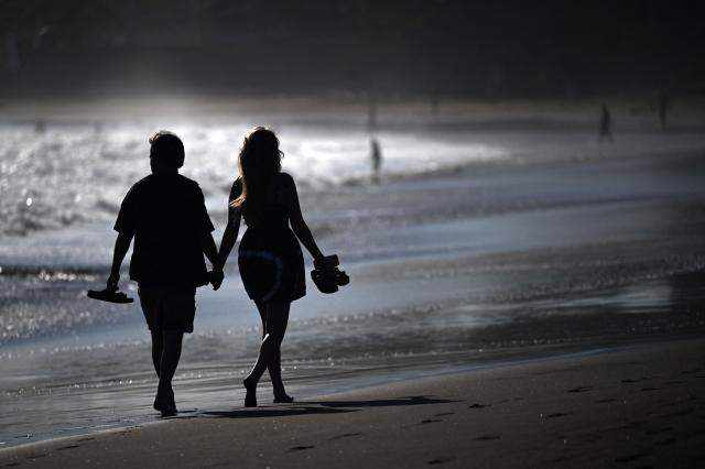A couple walks by the seashore at El Tunco beach, in La Libertad, El Salvador, on February 13, 2026. Amid picture-perfect waves and sunsets, foreign tourists enjoy the Salvadoran beach of El Tunco, once plagued by gang violence. They are full of praise for President Nayib Bukele, even though they admit that innocent people may have been caught up in his crackdown. (Photo by Marvin RECINOS / AFP)