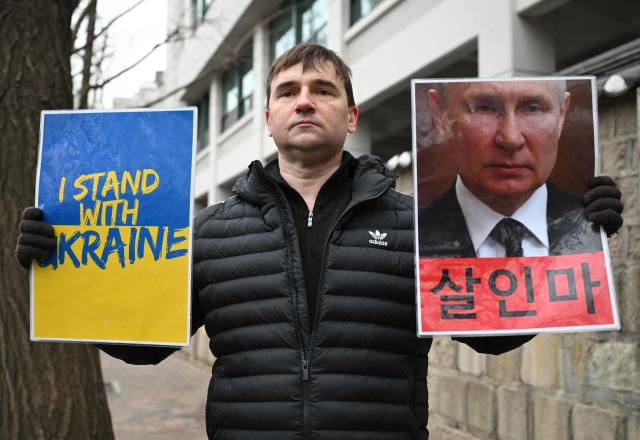 A Russian protester holds placards showing a picture of Russia's President Vladimir Putin (R) reading "Murderer" as he condemns Russia's invasion of Ukraine near the Russian embassy in Seoul on February 24, 2026, on the 4th anniversary of the Russia-Ukraine war. (Photo by Jung Yeon-je / AFP)
