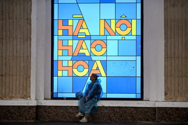 A woman sits in front of a billboard in Hanoi on February 24, 2026. (Photo by Nhac NGUYEN / AFP)