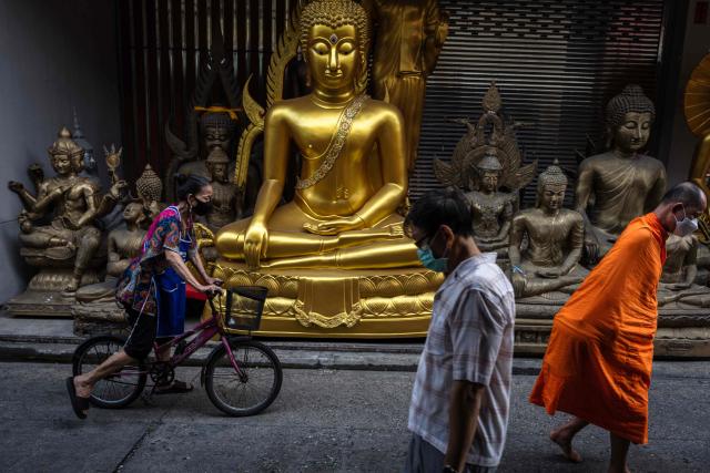 Pedestrians, including a monk, walk past a shop selling Buddha statues in Bangkok on February 24, 2026. (Photo by chanakarn laosarakham / AFP)
