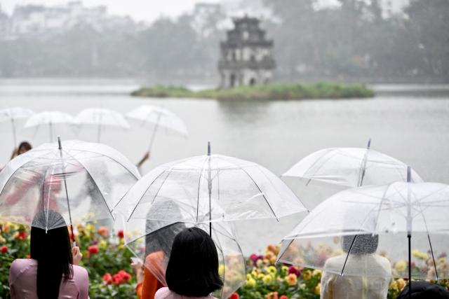 Women holding umbrellas stand beside Hoan Kiem Lake in Hanoi on February 24, 2026. (Photo by Nhac NGUYEN / AFP)