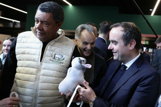 France's Prime Minister Sebastien Lecornu (R), holds the Salon de l'Agriculture 2026 edition mascot, named Biguine, next to its owner French Brahman cattle breeder from Martinique Andre Prosper during the Paris International Agricultural Show (Salon de l'Agriculture) at Paris Expo Porte de Versailles in Paris on February 24, 2026. (Photo by Alain JOCARD / AFP)