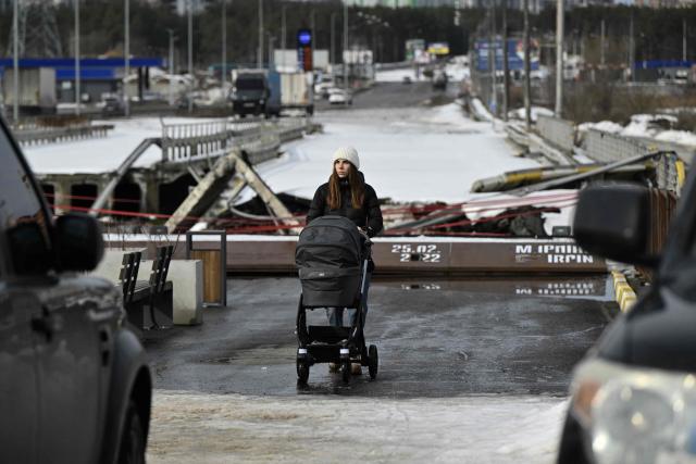 A woman with child stroller walks past memorial on a destroyed bridge in Irpin, northwest of Kyiv, on February 24, 2026, on the fourth anniversary of Russia's invasion of Ukraine. In 2022, many residents of Irpin, which was turned into a battlefield early in Russia's full-scale invasion, passed under the destroyed bridge in an attempt escape towards Kyiv. (Photo by Genya SAVILOV / AFP)