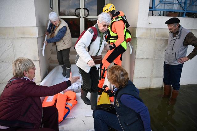 Firefighters assist elderly residents to climb into their boat as they are rescued from rising floodwaters following the passage of Storm Nils in Saintes, south-western France on February 24, 2026. The water continues to recede slowly in western France, according to Vigicrues, suggesting a gradual return to normal in some affected areas, just as the record for the longest period under red flood alert in France has been broken. (Photo by Christophe ARCHAMBAULT / AFP)