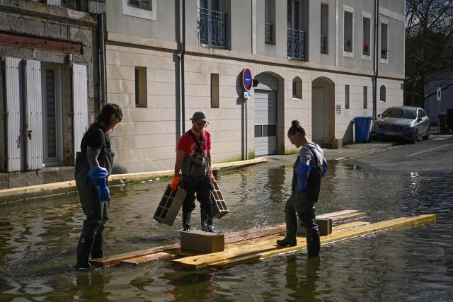 Residents use blocks and wooden planks to form walkways in rising floodwaters following the passage of Storm Nils in Saintes, south-western France on February 24, 2026. The water continues to recede slowly in western France, according to Vigicrues, suggesting a gradual return to normal in some affected areas, just as the record for the longest period under red flood alert in France has been broken. (Photo by Christophe ARCHAMBAULT / AFP)