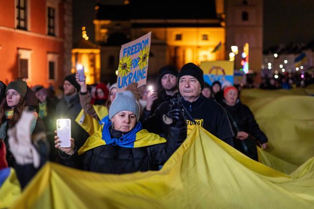 People hold a giant ukrainian flag as they take part in rally in support of Ukraine to mark 4th anniversary of the Russian full scale invasion on Ukraine  on February 24, 2026 in front of Royal Castle, in Warsaw's Old Town. (Photo by Wojtek RADWANSKI / AFP)