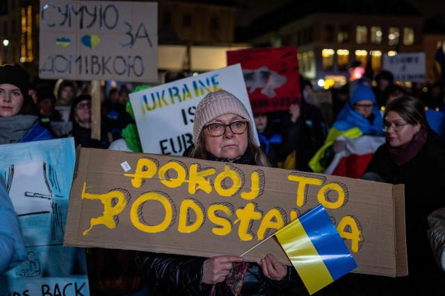 A woman holds a Ukrainian national flag and a banners reading "Peace is the foundation" as she takes part in rally in support of Ukraine to mark 4th anniversary of the Russian full scale invasion on Ukraine  on February 24, 2026 in front of Royal Castle, in Warsaw's Old Town. (Photo by Wojtek RADWANSKI / AFP)