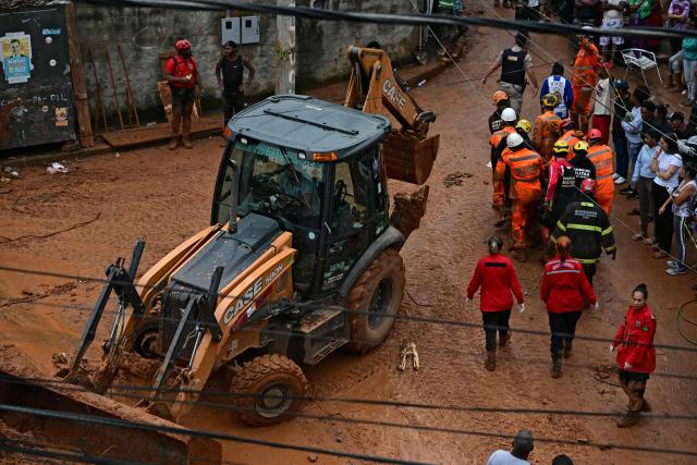 Rescue carry a corpse recovered from amid the debris past a backhoe loader after a landslide caused by heavy rains in the Barrio Parque Jardim Burnier neighbourhood in Juiz de Fora, Minas Gerais State, Brazil, on February 24, 2026. Torrential rains in southeastern Brazil have left at least 25 people dead and 43 missing after a river burst its banks and a wall of mud swept away houses in the middle of the night, officials said on February 24. (Photo by Pablo PORCIUNCULA / AFP)