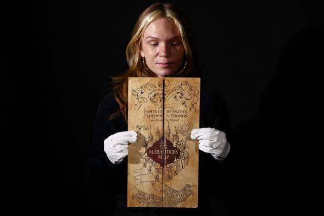 This photo taken on January 30, 2026 shows a gallery assistant posing with 'The Marauder’s Map' from the 2004 movie "Harry Potter and the Prisoner of Azkaban", at a preview by memorabilia auction house Propstore in Rickmansworth, near London. A collection of around 1,550 pieces of film and TV history will go under the hammer over three days from March 25, with in-room bidding on the first day only at the Petersen Automotive Museum in Los Angeles. (Photo by HENRY NICHOLLS / AFP)