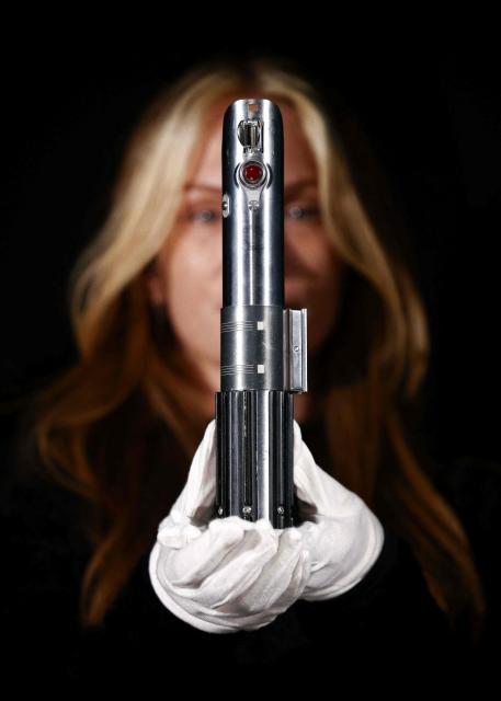 This photo taken on January 30, 2026 shows a gallery assistant posing with 'Rey and Luke Skywalker’s Hero Lightsaber' from the 2015 movie "Star Wars: The Force Awakens", at a preview by memorabilia auction house Propstore in Rickmansworth, near London. A collection of around 1,550 pieces of film and TV history will go under the hammer over three days from March 25, with in-room bidding on the first day only at the Petersen Automotive Museum in Los Angeles. (Photo by HENRY NICHOLLS / AFP)