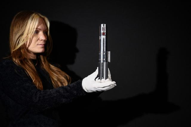 This photo taken on January 30, 2026 shows a gallery assistant posing with 'Rey and Luke Skywalker’s Hero Lightsaber' from the 2015 movie "Star Wars: The Force Awakens", at a preview by memorabilia auction house Propstore in Rickmansworth, near London. A collection of around 1,550 pieces of film and TV history will go under the hammer over three days from March 25, with in-room bidding on the first day only at the Petersen Automotive Museum in Los Angeles. (Photo by HENRY NICHOLLS / AFP)