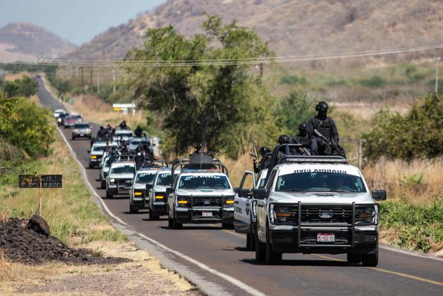 TOPSHOT - Members of the Civil Guard of Michoacan patrol a highway supported by armored vehicles after a wave of violence in the town of Aguililla, the birthplace of drug kingpin Nemesio Oseguera, leader of the Jalisco New Generation Cartel (CJNG) in Tierra Caliente, Mexico, on February 24, 2026. Mexican President Claudia Sheinbaum on February 24 dismissed risks to fans visiting Guadalajara, one of the venues for the 2026 World Cup, after a drug cartel riot caused fear in the city and much of the country on February 22. (Photo by Enrique Castro / AFP)