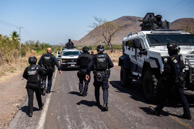 Members of the Civil Guard of Michoacan patrol a highway supported by armored vehicles after a wave of violence in the town of Aguililla, the birthplace of drug kingpin Nemesio Oseguera, leader of the Jalisco New Generation Cartel (CJNG) in Tierra Caliente, Mexico, on February 24, 2026. Mexican President Claudia Sheinbaum on February 24 dismissed risks to fans visiting Guadalajara, one of the venues for the 2026 World Cup, after a drug cartel riot caused fear in the city and much of the country on February 22. (Photo by Enrique Castro / AFP)