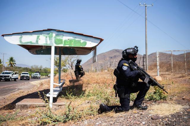 Members of the Civil Guard of Michoacan patrol a highway supported by armored vehicles after a wave of violence in the town of Aguililla, the birthplace of drug kingpin Nemesio Oseguera, leader of the Jalisco New Generation Cartel (CJNG) in Tierra Caliente, Mexico, on February 24, 2026. Mexican President Claudia Sheinbaum on February 24 dismissed risks to fans visiting Guadalajara, one of the venues for the 2026 World Cup, after a drug cartel riot caused fear in the city and much of the country on February 22. (Photo by Enrique Castro / AFP)