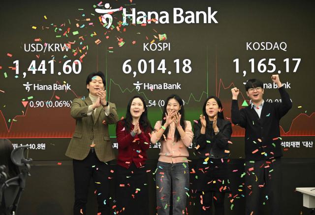 Currency dealers celebrate South Korea's benchmark stock index breaking the 6,000 points during a ceremony in a foreign exchange dealing room at the Hana Bank headquarters in Seoul on February 25, 2026. South Korea's benchmark Kospi index topped 6,000 points for the first time on February 25, buoyed by the strong performance of the nation's world-leading semiconductor industry. (Photo by Jung Yeon-je / AFP)