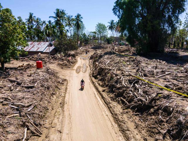 An aerial view shows a person riding a motorcycle past flash flood damage at a residential area in Meurah Dua, Aceh province's Pidie Jaya district on February 22, 2026, after devastating floods and landslides struck Indonesia's Sumatra late last year. Some 32,000 flood survivors remain displaced following the late 2025 monsoon deluge. In hardest-hit Aceh province, which accounted for most of the more than 1,000 deaths, families have become increasingly frustrated over authorities' sluggish response. Many remain crammed in temporary shelters or a cluster of tents, with little expectation of returning to their mud-caked homes any time soon. (Photo by CHAIDEER MAHYUDDIN / AFP) / To go with AFP story Indonesia-flood by Alfath Asmunda