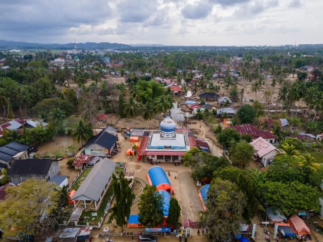 An aerial view shows tents (in orange and blue), used as temporary housing by flood survivors, erected in the compounds of a mosque in Meurah Dua, Aceh province's Pidie Jaya district on February 21, 2026, after devastating floods and landslides struck Indonesia's Sumatra late last year. Some 32,000 flood survivors remain displaced following the late 2025 monsoon deluge. In hardest-hit Aceh province, which accounted for most of the more than 1,000 deaths, families have become increasingly frustrated over authorities' sluggish response. Many remain crammed in temporary shelters or a cluster of tents, with little expectation of returning to their mud-caked homes any time soon. (Photo by CHAIDEER MAHYUDDIN / AFP) / To go with AFP story Indonesia-flood by Alfath Asmunda