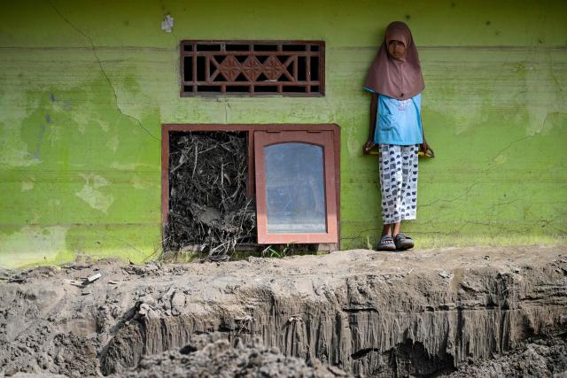A child stands on hardened mud beside the window of a residence damaged by flash floods in Meurah Dua, Aceh province's Pidie Jaya district on February 21, 2026, after devastating floods and landslides struck Indonesia's Sumatra late last year. Some 32,000 flood survivors remain displaced following the late 2025 monsoon deluge. In hardest-hit Aceh province, which accounted for most of the more than 1,000 deaths, families have become increasingly frustrated over authorities' sluggish response. Many remain crammed in temporary shelters or a cluster of tents, with little expectation of returning to their mud-caked homes any time soon. (Photo by CHAIDEER MAHYUDDIN / AFP) / To go with AFP story Indonesia-flood by Alfath Asmunda