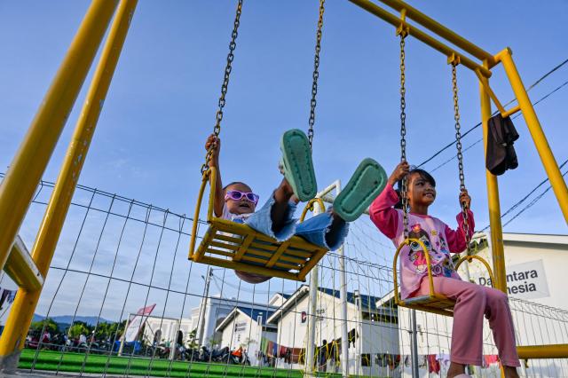 Children ride swings at a playground in temporary housing for flood survivors in Meureudu, Aceh province's Pidie Jaya district on February 22, 2026, after devastating floods and landslides struck Indonesia's Sumatra late last year. Some 32,000 flood survivors remain displaced following the late 2025 monsoon deluge. In hardest-hit Aceh province, which accounted for most of the more than 1,000 deaths, families have become increasingly frustrated over authorities' sluggish response. Many remain crammed in temporary shelters or a cluster of tents, with little expectation of returning to their mud-caked homes any time soon. (Photo by CHAIDEER MAHYUDDIN / AFP) / To go with AFP story Indonesia-flood by Alfath Asmunda