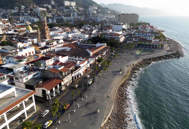 This aerial view shows people walking on the coastline of Puerto Vallarta, Jalisco state, Mexico on February 24, 2026. Known as a sunny tourist paradise, parts of the coastal city of Puerto Vallarta seem more like the set of a war film in the aftermath of violent chaos spurred by the capture and death of Mexico's most-wanted drug lord Nemesio "El Mencho" Oseguera. (Photo by Alfredo ESTRELLA / AFP)