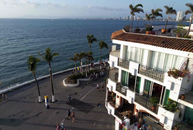 This aerial view shows people walking on the coastline of Puerto Vallarta, Jalisco state, Mexico on February 24, 2026. Known as a sunny tourist paradise, parts of the coastal city of Puerto Vallarta seem more like the set of a war film in the aftermath of violent chaos spurred by the capture and death of Mexico's most-wanted drug lord Nemesio "El Mencho" Oseguera. (Photo by Alfredo ESTRELLA / AFP)