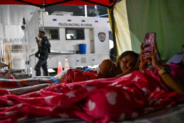 Relatives of political prisoners sleep on a tent set up in front of Bolivarian national police officers during a protest outside the Zone 7 prison of the Bolivarian National Police (PNB) in Caracas on February 24, 2026. A total of 179 political prisoners were released from prison in Venezuela under the recently enacted amnesty law, Parliament reported on February 24, as complaints mount about delays in processing the benefit in the courts. (Photo by Juan BARRETO / AFP)