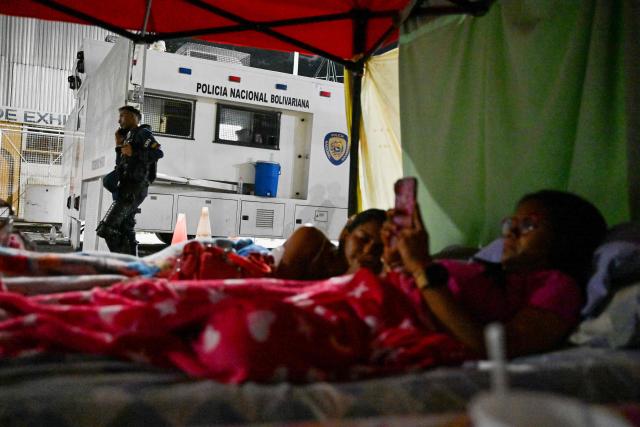 Relatives of political prisoners sleep on a tent set up in front of Bolivarian national police officers during a protest outside the Zone 7 prison of the Bolivarian National Police (PNB) in Caracas on February 24, 2026. A total of 179 political prisoners were released from prison in Venezuela under the recently enacted amnesty law, Parliament reported on February 24, as complaints mount about delays in processing the benefit in the courts. (Photo by Juan BARRETO / AFP)