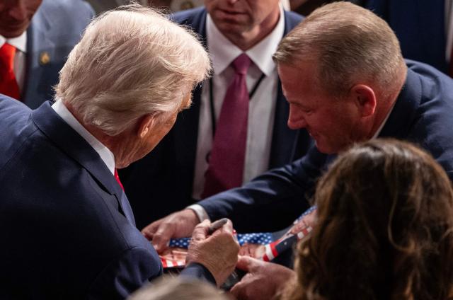 US President Donald Trump signs a guest's tie at his effigy as he departs the House Chamber of the US Capitol in Washington after delivering the State of the Union address, February 24, 2026. (Photo by ANDREW CABALLERO-REYNOLDS / AFP)