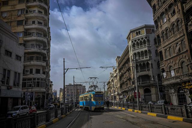 A man walks alonside a tram in the coastal city of Alexandria on February 18, 2026. Along Egypt's Mediterranean coast, the oldest tram in Africa and the Middle East rumbles for a final few weeks before its removal -- the latest urban upheaval Alexandrians say is hollowing out their city's identity. Inaugurated in 1863, the tram is one of the world's oldest, and among only a few to operate double-decker cars. (Photo by Khaled DESOUKI / AFP)